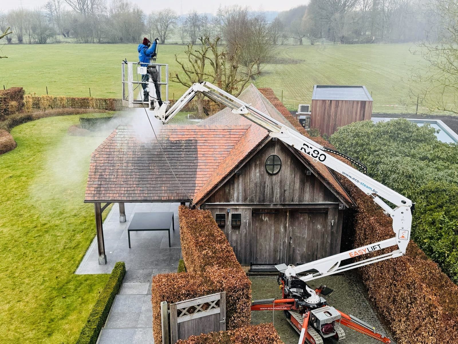 Luchtbeeld van een dakreiniging met de hoogtewerker naast de woning
