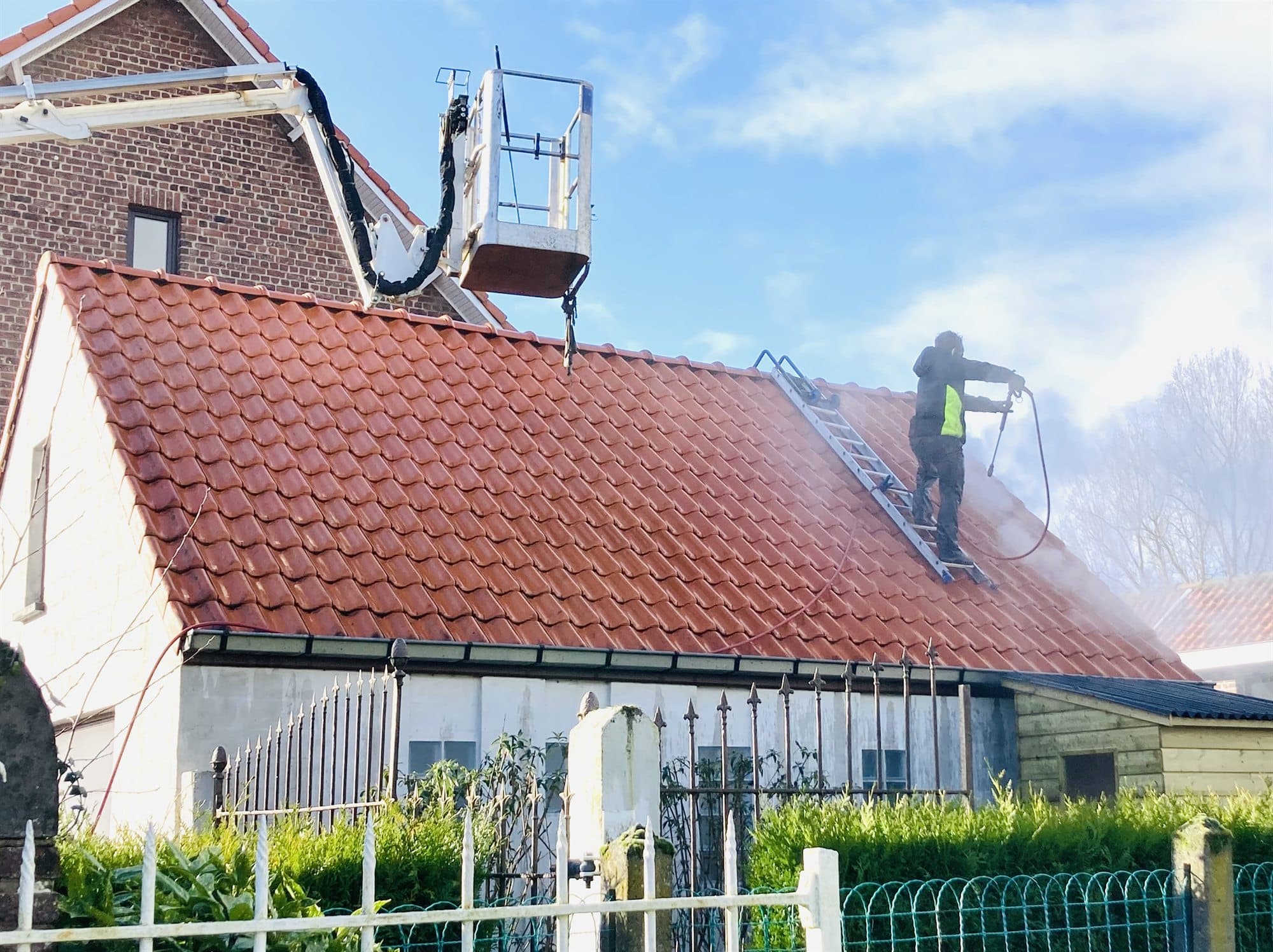 Medewerker van Eco-Steam reinigt het dak van een hoeve, met de hoogtewerker ernaast